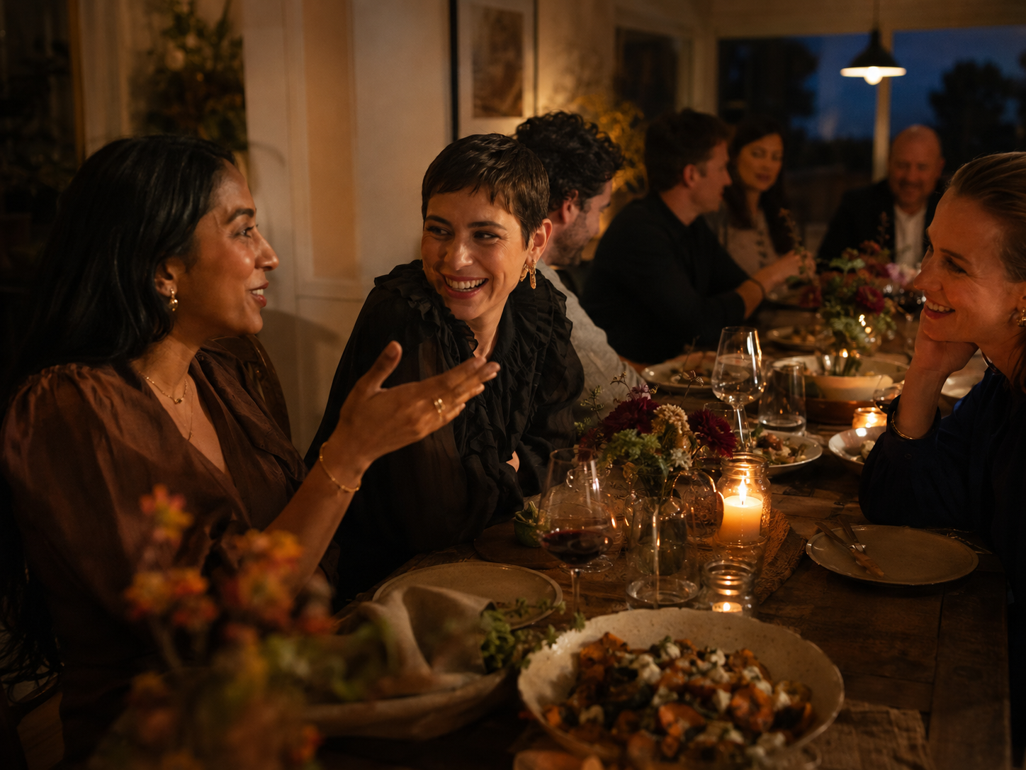 Three guests absorbed in a warm, animated conversation while the rest of the dinner continues around them.